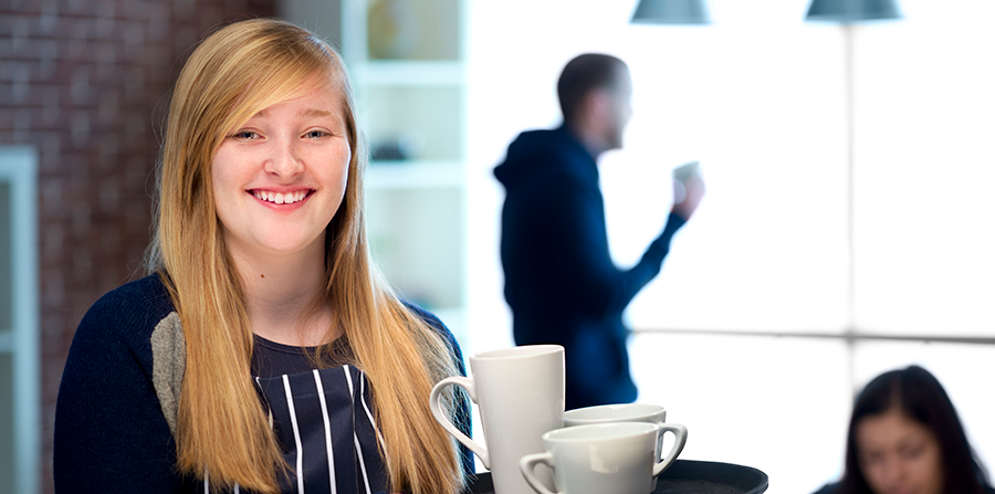 Young female waitress carrying a tray of coffees and smiling at the camera