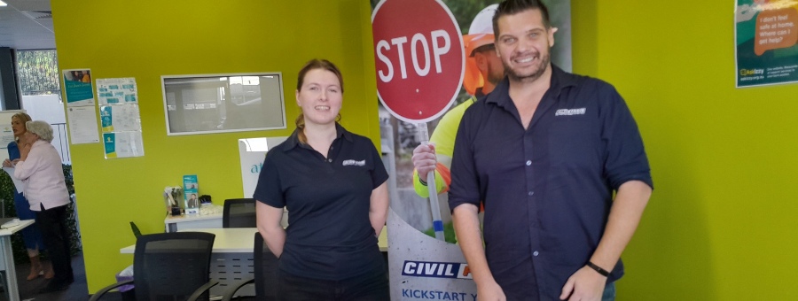 Two people stand in front of a pull up banner with a stop sign promoting civil construction training